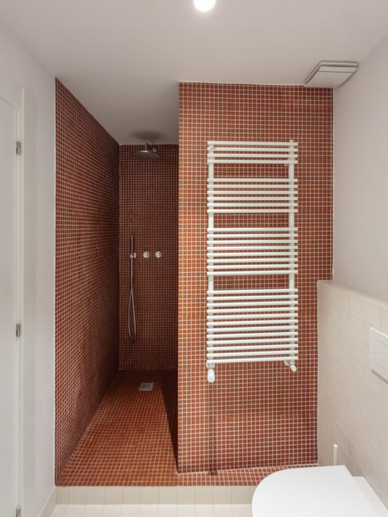 Baño de Casa Vega con gresite granate y radiador toallero, con grifería empotrada de acero cepillado