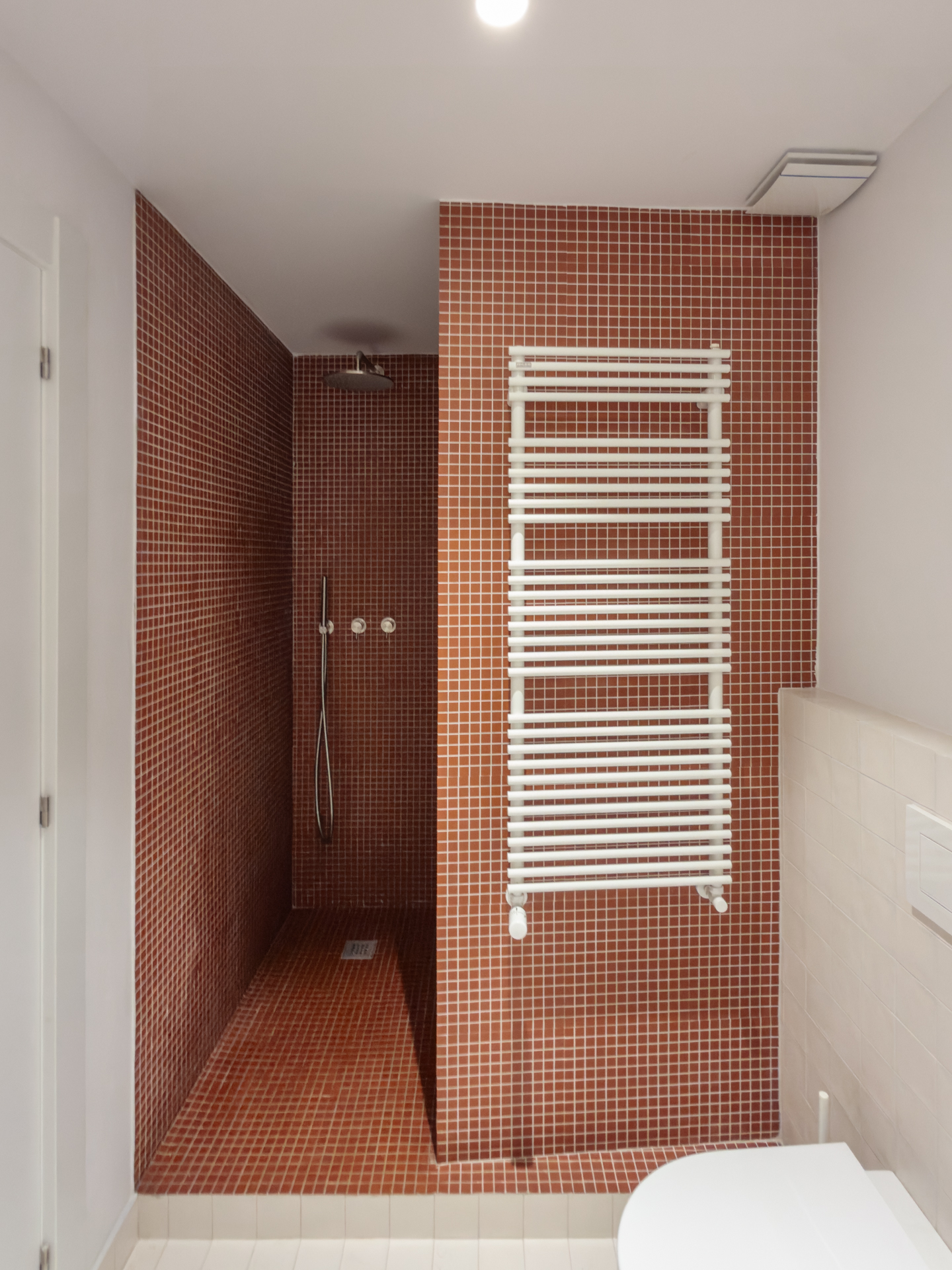 Baño de Casa Vega con gresite granate y radiador toallero, con grifería empotrada de acero cepillado